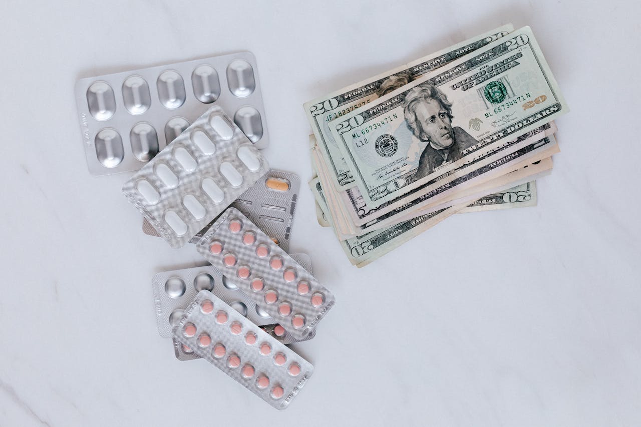 Blister packs of pills and US dollars on a white surface.